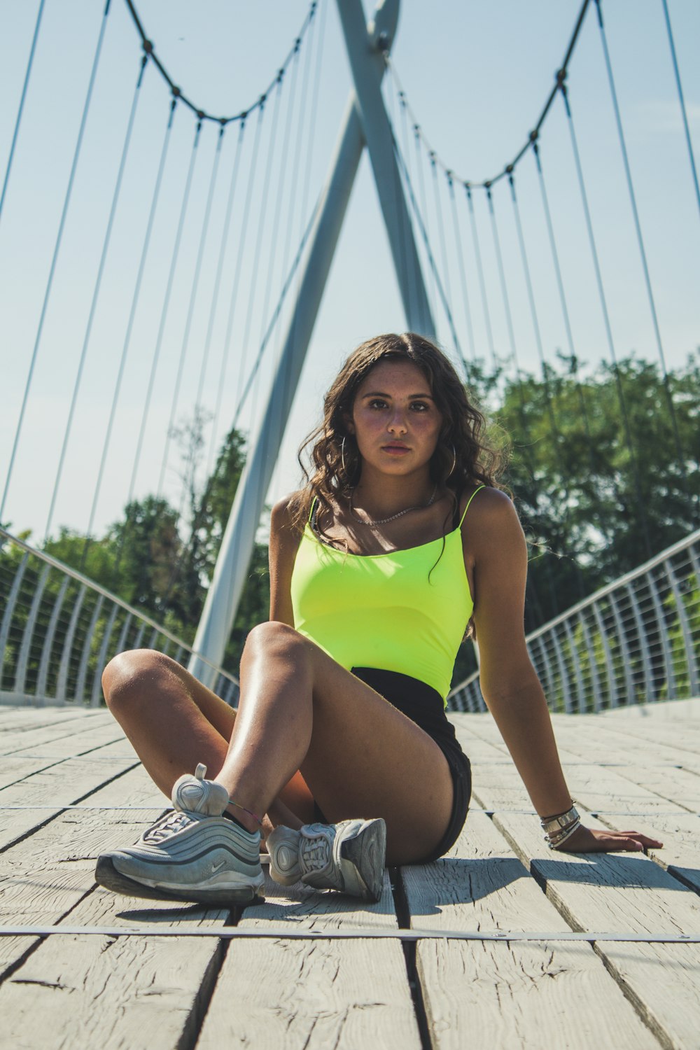 woman in green spaghetti strapped top sitting on wooden suspension bridge