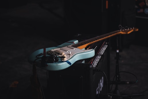 Vintage electric guitar resting against an old amplifier in a dimly lit room.
