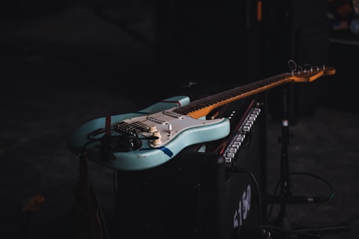 Electric guitar resting on a neon-lit amplifier in a shadowy room.