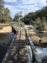Hikers crossing a wooden bridge over a clear mountain stream surrounded by lush greenery.