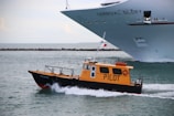 a yellow and black boat in the water and a large ship in the background