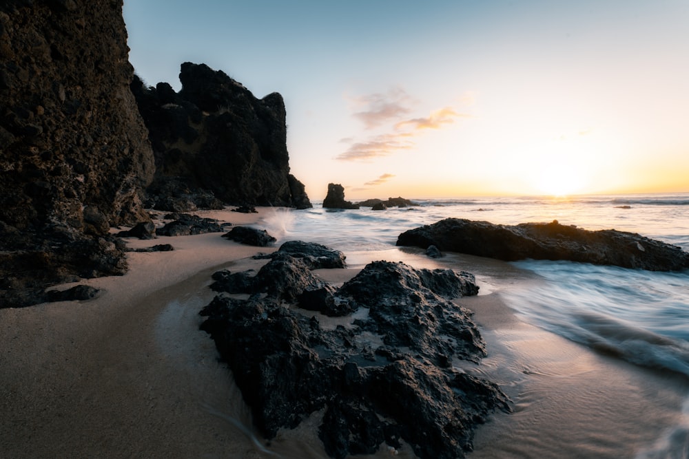 the sun is setting over the ocean and rocks