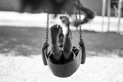 grayscale-photography of boy playing swing chair