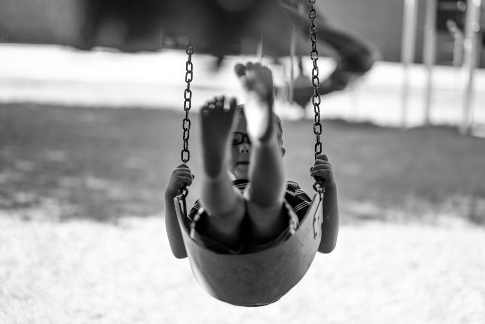 grayscale-photography of boy playing swing chair