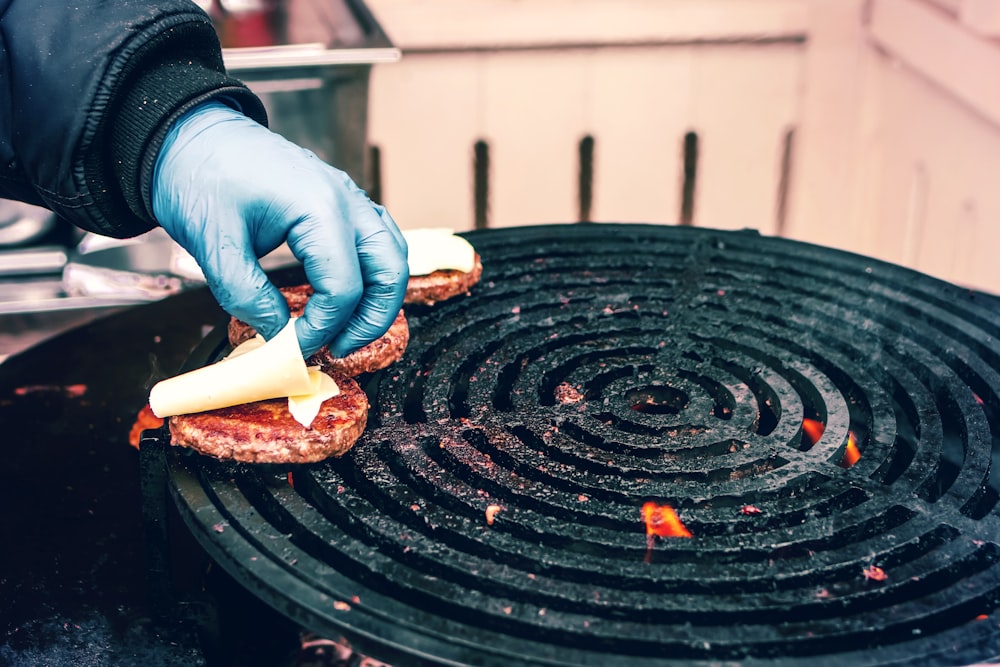 person placing cheese on brown patties on grill