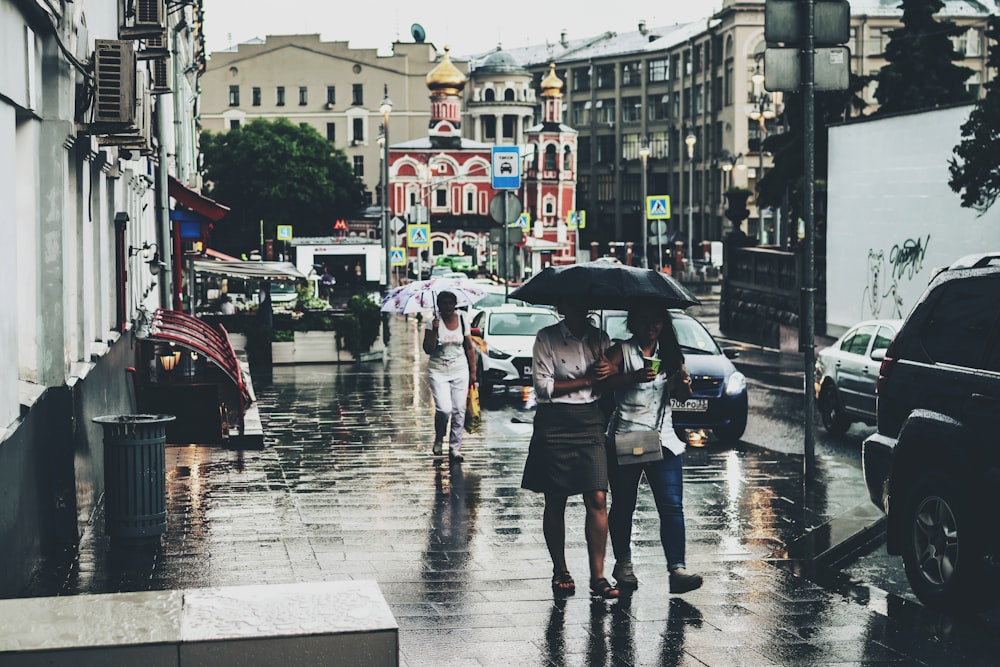 우산을 쓴 세 명의 여성이 비를 맞으며 보도를 걷고 있습니다.