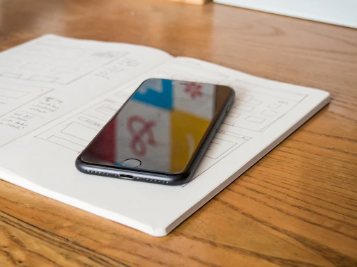 A friendly office desk with a smartphone displaying a colorful app interface and a notebook with sketches.