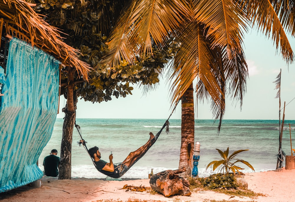 man on hammock while using smartphone beside seashore