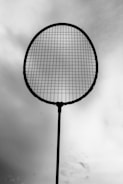 A silhouetted tennis racket is held against a cloudy sky, with the strings clearly visible.