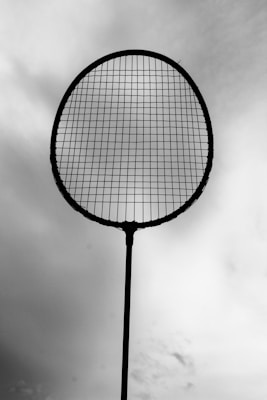 A silhouetted tennis racket is held against a cloudy sky, with the strings clearly visible.