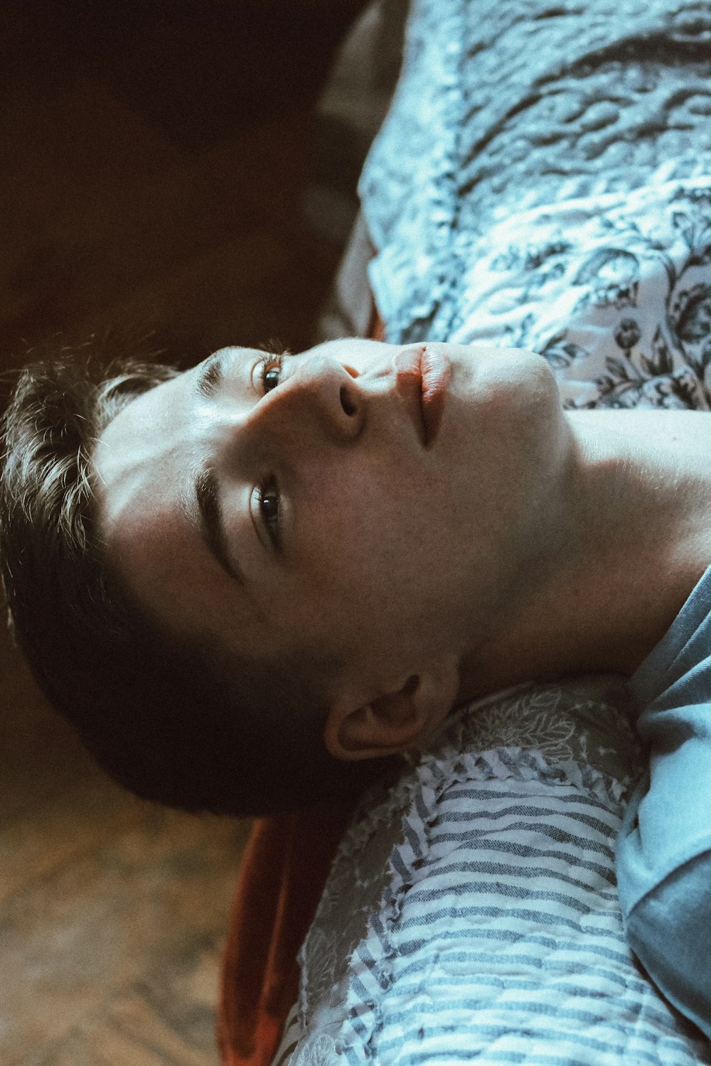 person wearing gray shirt lying on white and gray floral textile
