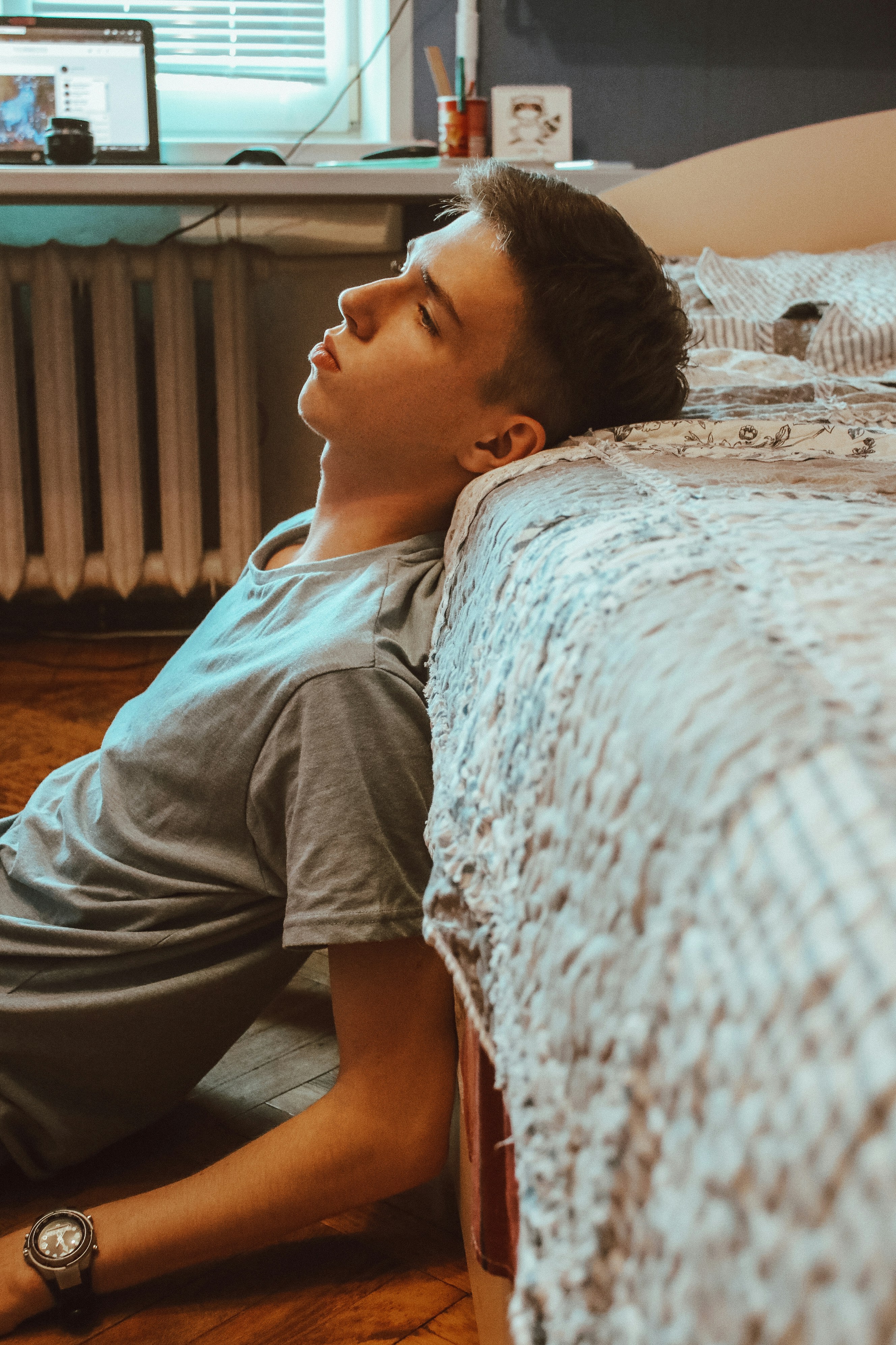 A young man sitting on the floor near a bed, contemplating the impacts of exercise sleep before bedtime.