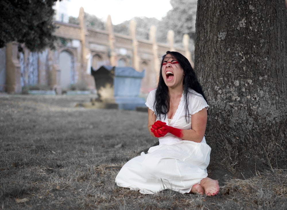 woman wearing white dress sitting besides brown tree