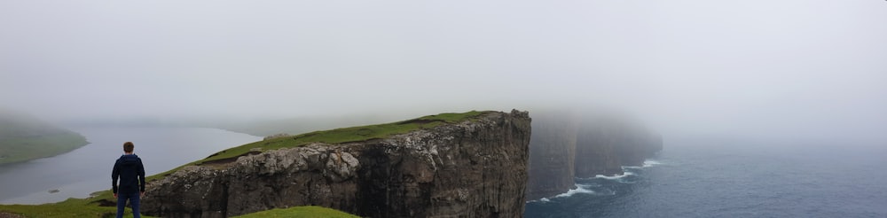 man standing on top of mountain facing on seashore during daytime