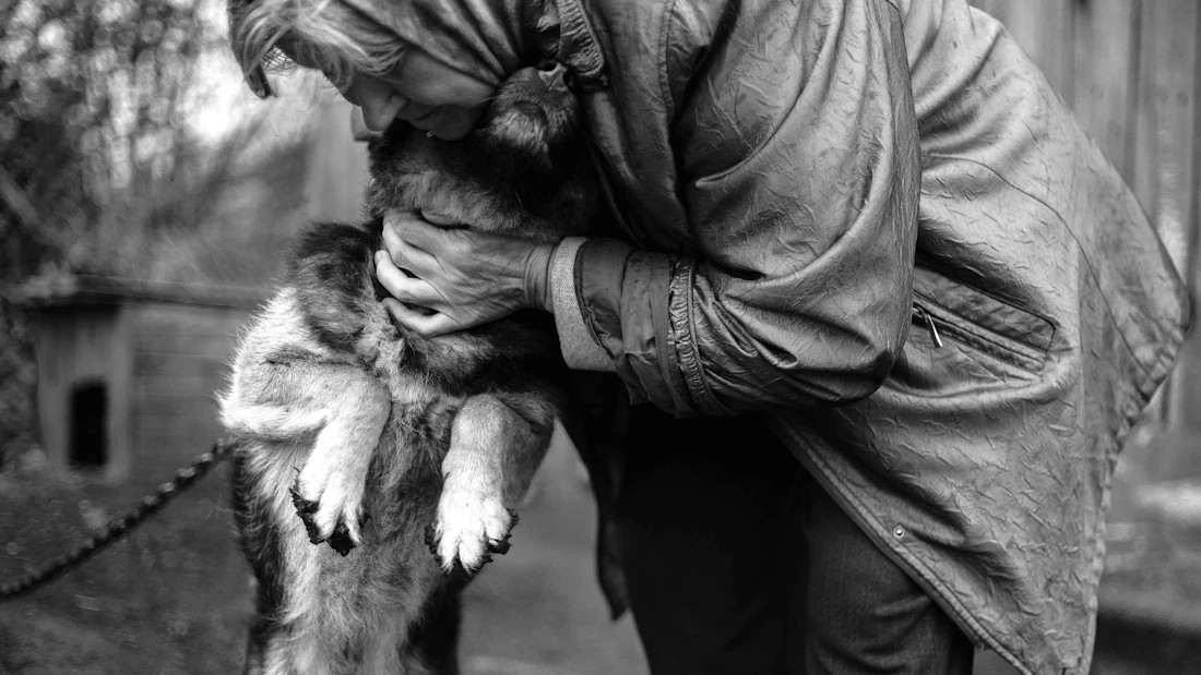 A woman tenderly hugging a calm dog close to her face during a quiet visit, in black and white