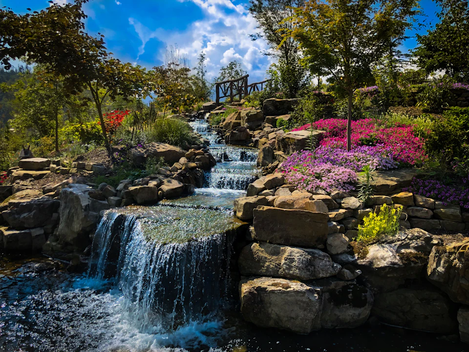 Serene garden scene featuring cascading waterfall surrounded by colorful flowers and lush foliage