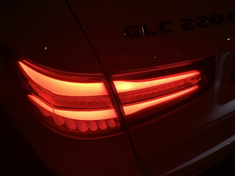 Red LED taillights of a vehicle, specifically a Mercedes GLC 220d, illuminated in the darkness with a glowing effect. The tailgate has embossed model lettering visible above the lights.