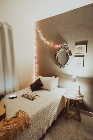 Cozy college dorm room with string lights, mirror, and neutral bedding