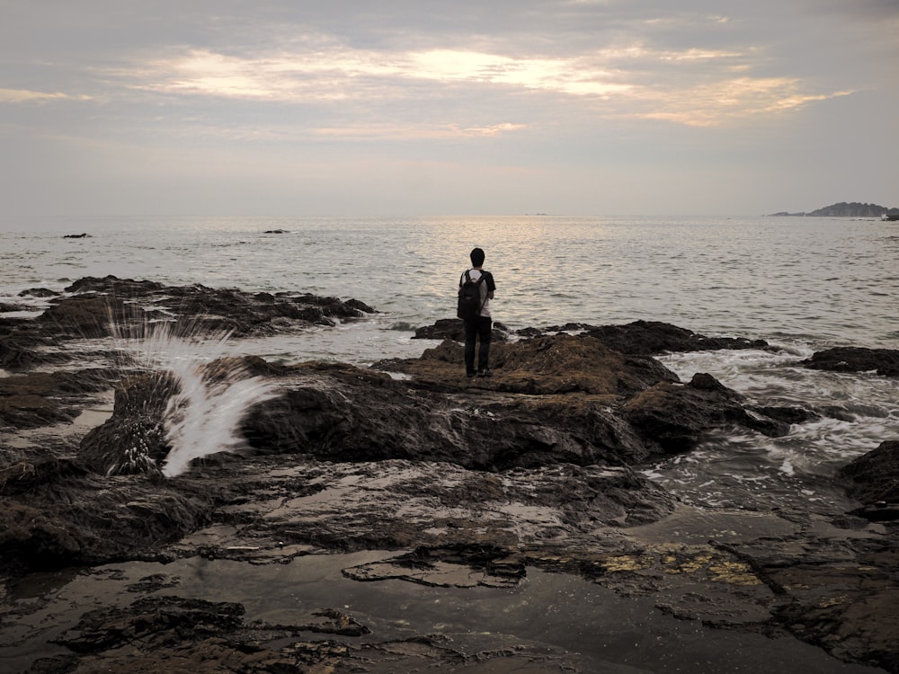 man standing on rock near ocean waves during daytime