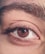A close-up of a human eye with detailed focus on the iris, eyelashes, and eyebrow. The skin texture and individual eyebrow hairs are visible, highlighting intricate details.