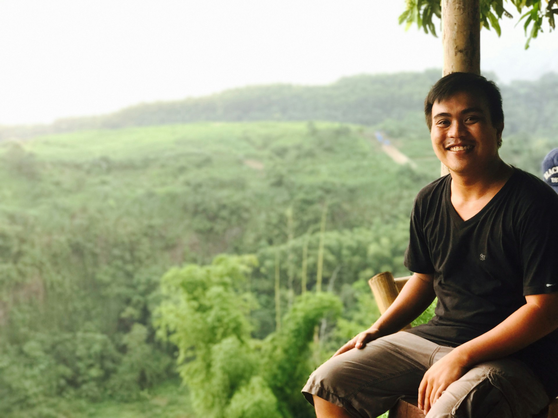 A smiling individual sitting outdoors with a tablet, surrounded by nature, representing freedom and ease gained through personal growth and steady income.