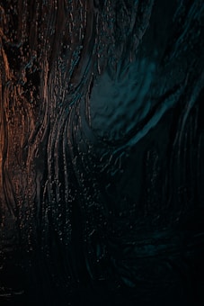 A textured surface with dark and rich colors, possibly resembling a wet or glossy material with light reflections.