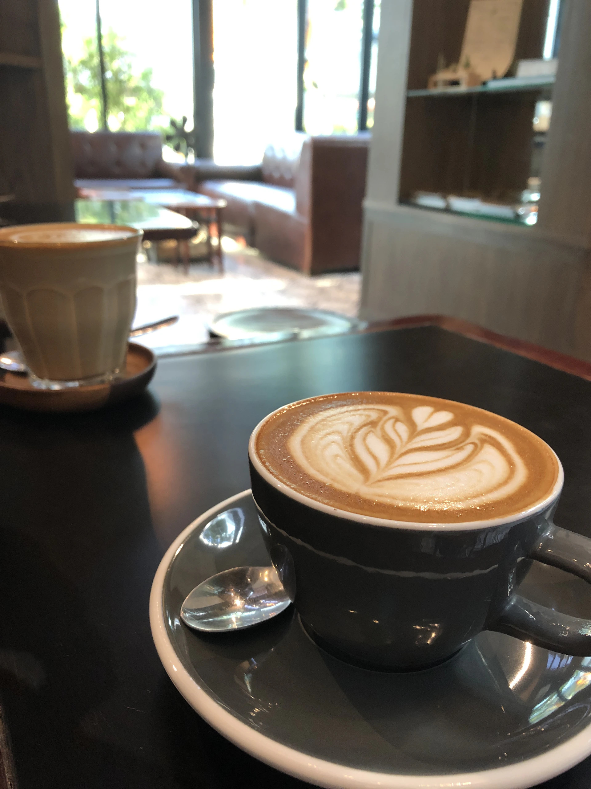 Close-up of a beautifully crafted coffee drink with latte art in a cozy, bright café setting featuring accents of yellow and purple.