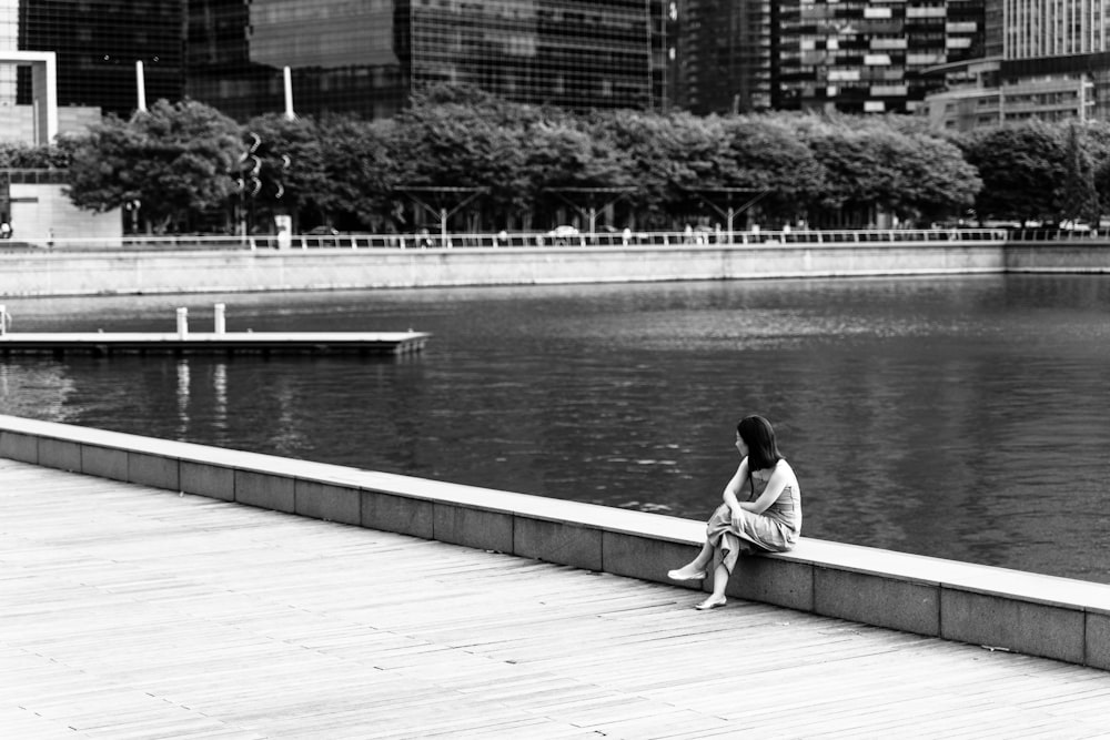 grayscale photography of woman sitting near body f water