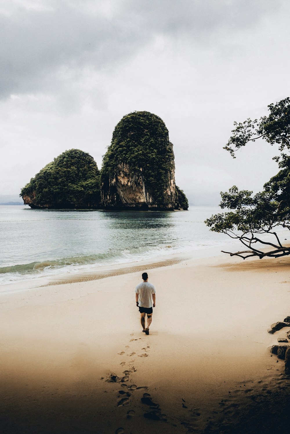 白いTシャツを着た男が2つの小島に面して海岸を歩く