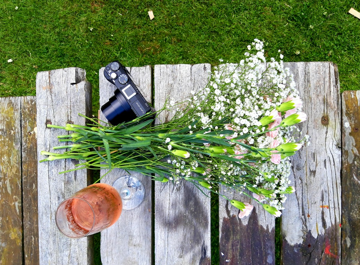 Bouquet of flowers, a glass of drink, and a DSLR camera on a table, symbolizing spring activities and creativity.