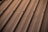 A section of a metal roof characterized by parallel lines and screws securing the panels. The surface appears smooth and reflects a warm, golden hue likely from sun exposure.