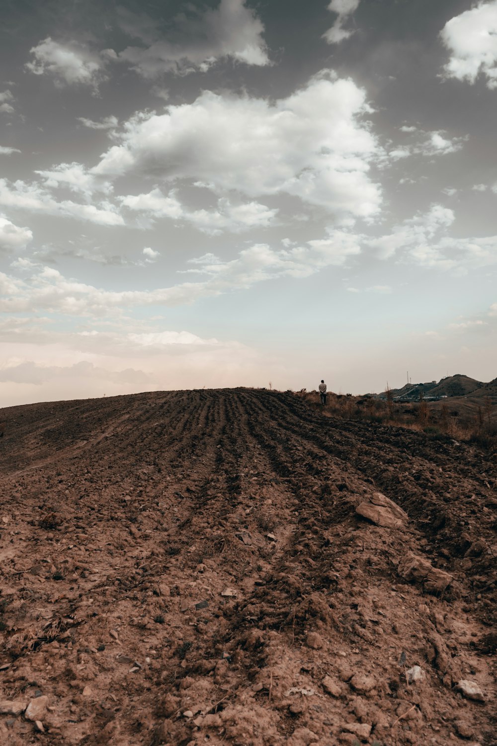 a dirt field with a sky filled with clouds