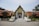 A traditional Thai temple with a richly decorated gable and intricate golden carvings is flanked by two large golden statues, likely mythical creatures, at the entrance. The temple features red-tiled roofs and lush greenery in the surroundings, with signs in Thai script.
