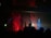 A dimly lit nightclub scene with two silhouetted DJs standing behind a console, surrounded by vibrant red and blue stage lights. The background features a series of spotlights and a light fog filling the space, creating a lively and energetic atmosphere.