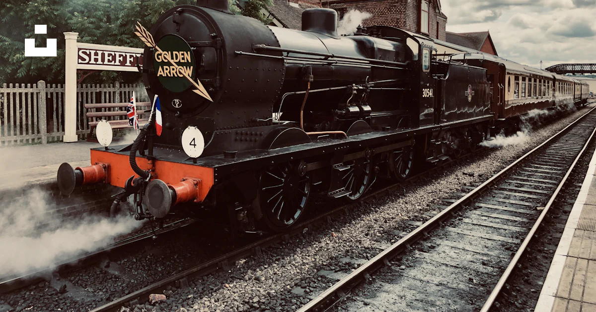 A black train traveling down train tracks next to a building photo ...