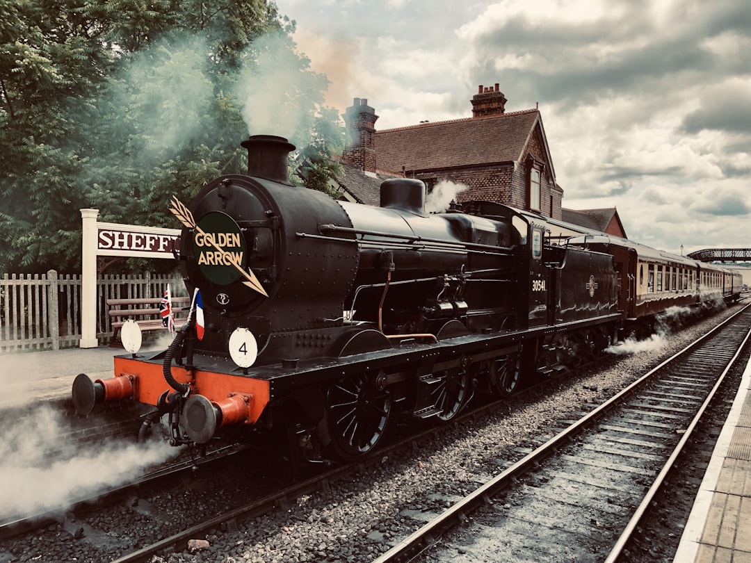 a black train traveling down train tracks next to a building, Taken at the Bluebell Railway.