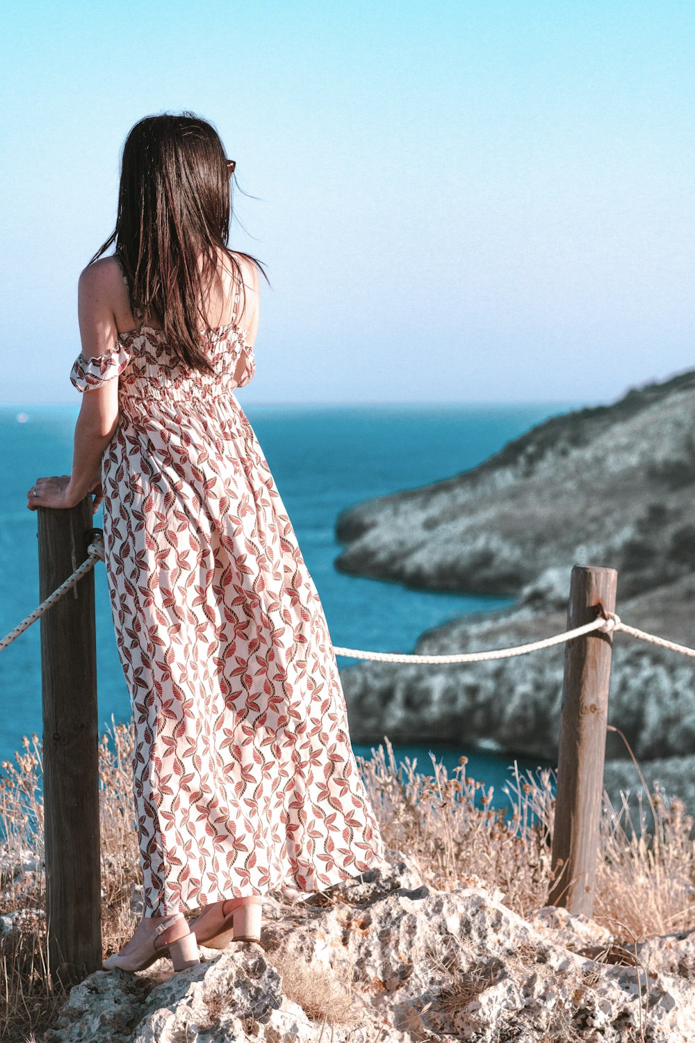 woman standing beside posts with ropes facing the sea