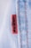 A close-up view of a denim fabric with prominent stitching details. A small red tag with black text is visible, partially showing a brand name. The fabric texture and stitching are clearly defined, illustrating the quality and craftsmanship of the material.