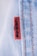 A close-up view of a denim fabric with prominent stitching details. A small red tag with black text is visible, partially showing a brand name. The fabric texture and stitching are clearly defined, illustrating the quality and craftsmanship of the material.