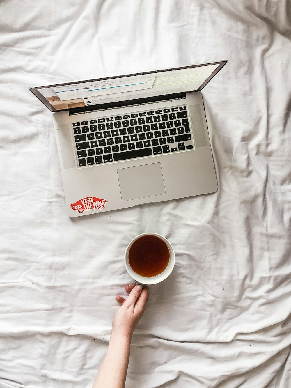 a person holding a cup of tea in front of a laptop