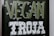 The image features a blackboard-style sign with bold lettering. The word 'VEGAN' is written in a light green color with small leaf accents around it, and the word 'TROJA' is below in bold white letters with a decorative font.