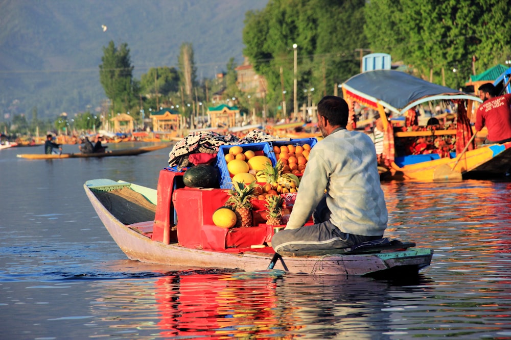 man sitting on boat selling different fruits