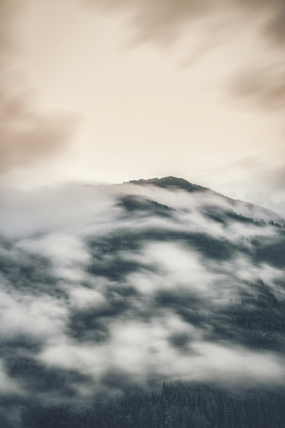 a mountain covered in fog and clouds under a cloudy sky