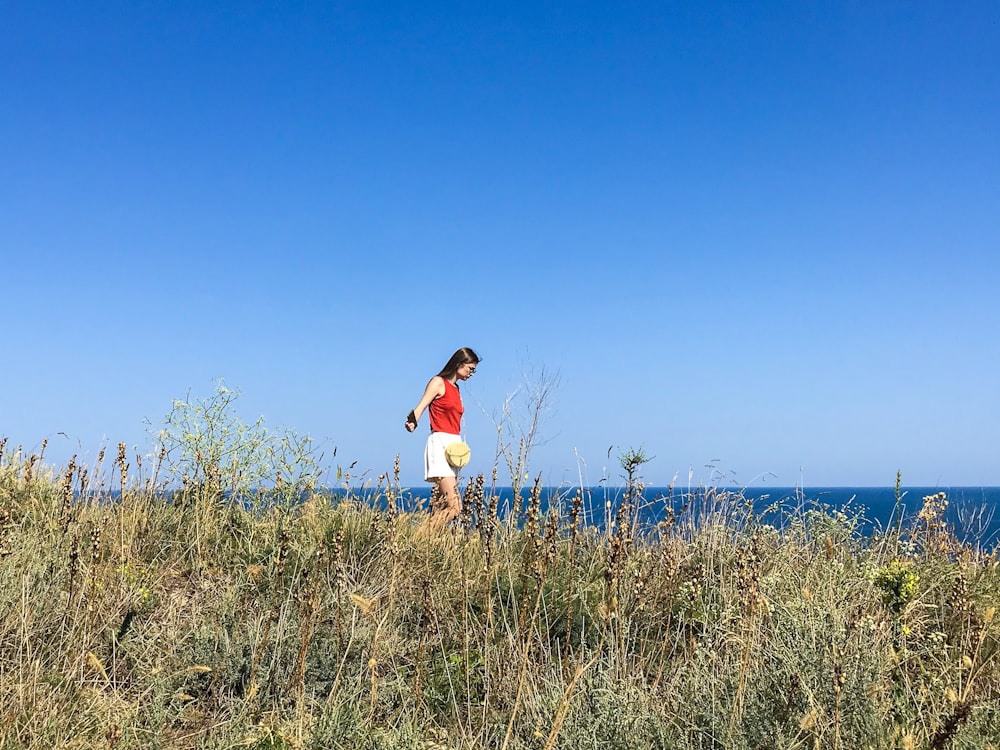 빨간 셔츠를 입은 여자가 바다 근처 잔디밭을 걷고 있다