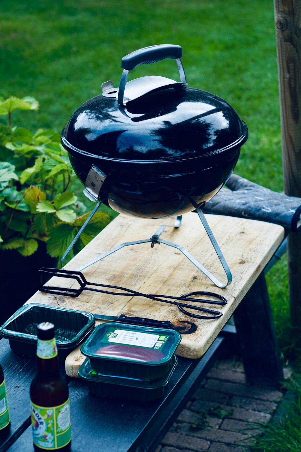 black portable kettle grill on top of wooden chopping board beside black tongs