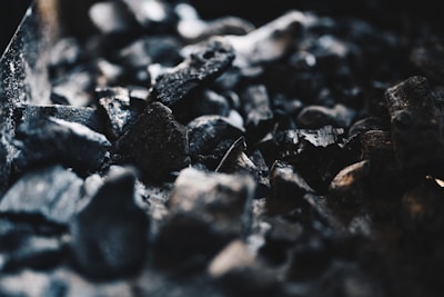 A close-up view of several pieces of coal or charcoal with rough and uneven textures. The image focuses on the dark, black tones of the material, with some highlights catching the light, creating a stark contrast against the shadows.