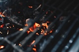 A close-up view of glowing charcoal embers under the grates of a barbecue grill, capturing the heat and energy of the burning coals.