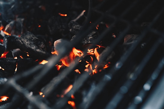 Close-up of a sizzling barbecue grill with glowing embers and smoke rising.