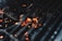 A close-up view of glowing charcoal embers under the grates of a barbecue grill, capturing the heat and energy of the burning coals.