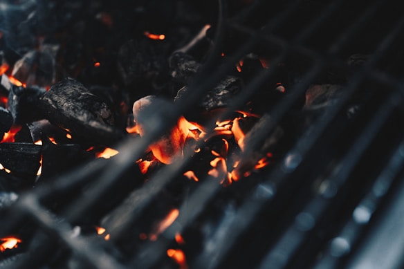 A close-up view of glowing charcoal embers under the grates of a barbecue grill, capturing the heat and energy of the burning coals.